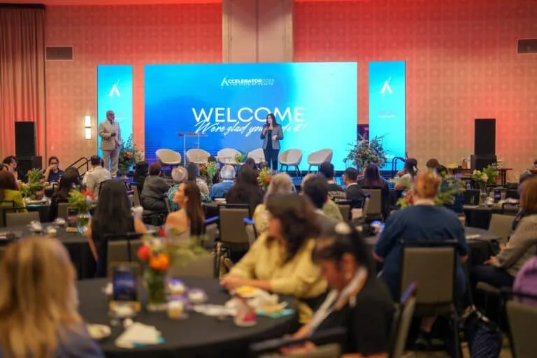 Attendees fill banquet tables facing the illuminated Accelerator stage.