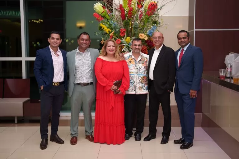 Guests gather for a group photo beside a floral arrangement.